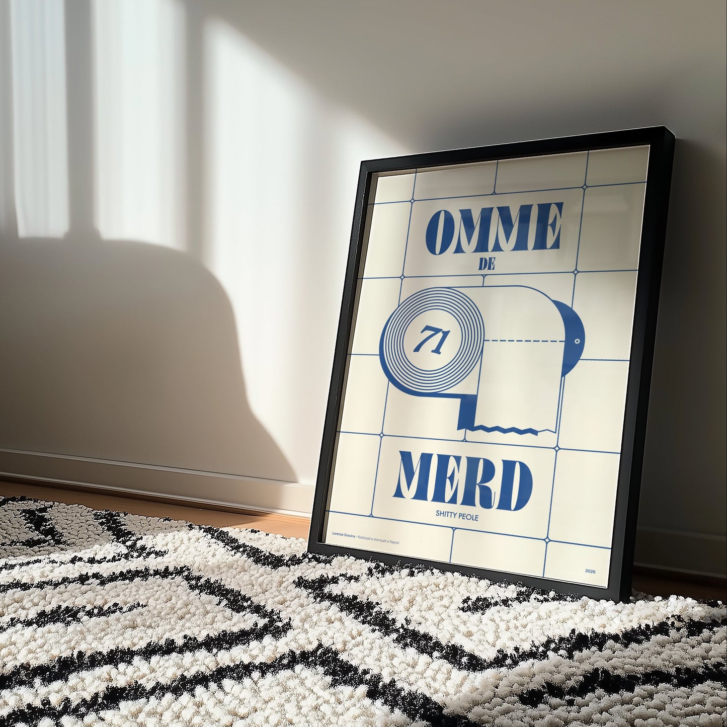 Poster Omme de Merd incorniciato accanto a poltrona crema e tappeto berbero — Posteria Verace, stampa napoletana