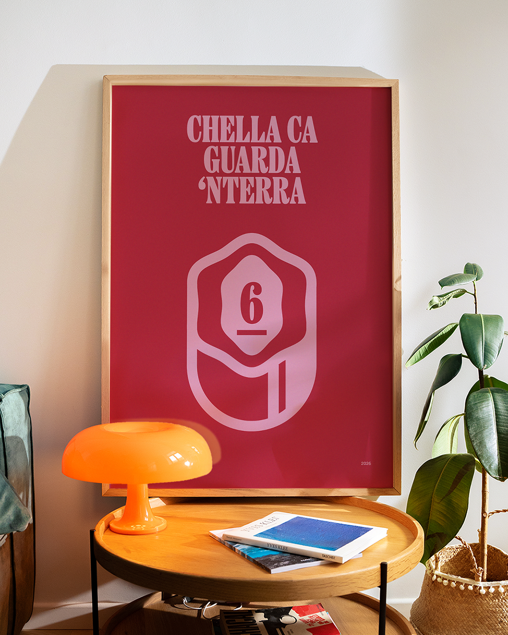 Poster Smorfia 6 «Chella ca guarda 'nterra» in cornice di legno chiaro appoggiato in camera da letto, sopra un tavolino con lampada arancione e pianta